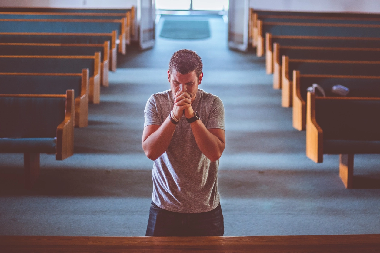 A man kneeling down in front of pews praying.